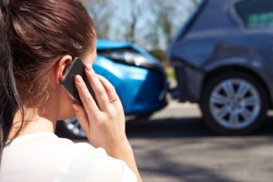 A woman talking on the phone while standing near a car accident